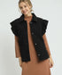 Woman wearing a black quilted vest over a brown dress on a light gray background