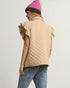Person wearing a beige quilted vest, blue jeans, and a pink knit beanie on a light gray background