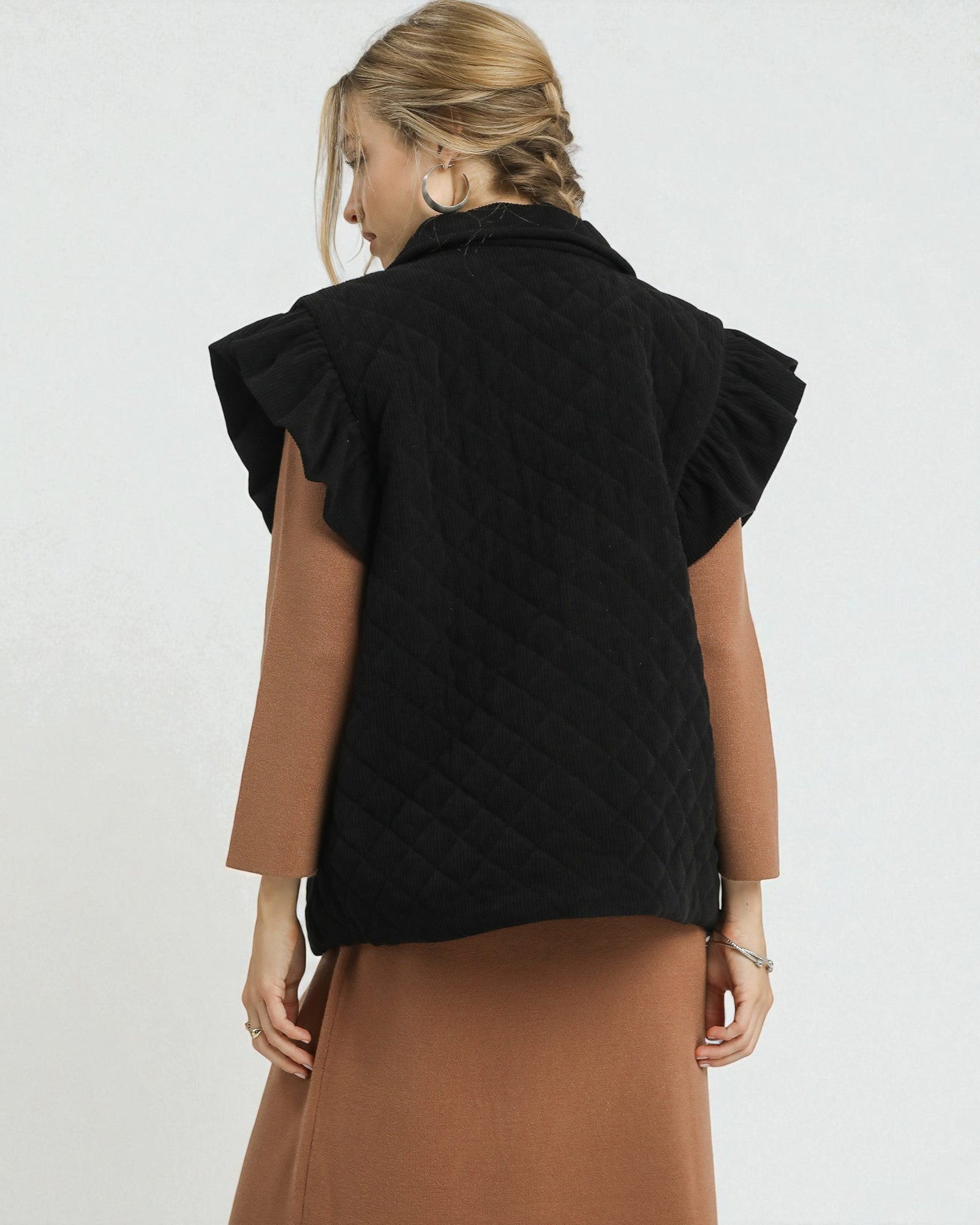 Woman wearing a black quilted vest over a brown dress on a white background