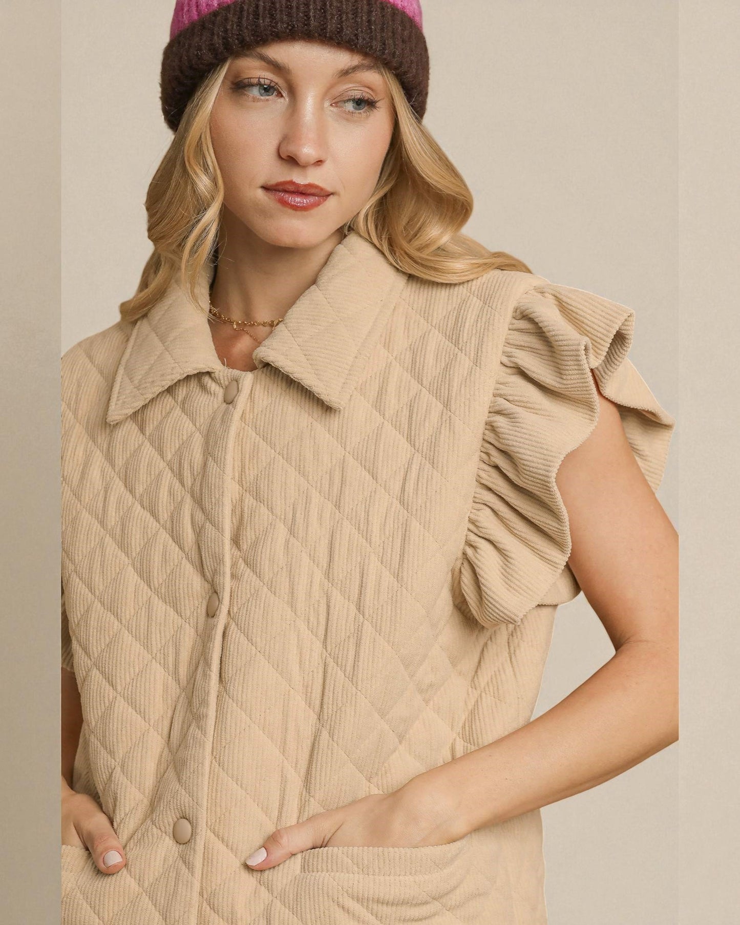 Woman wearing a beige quilted vest and pink knit hat against a neutral background