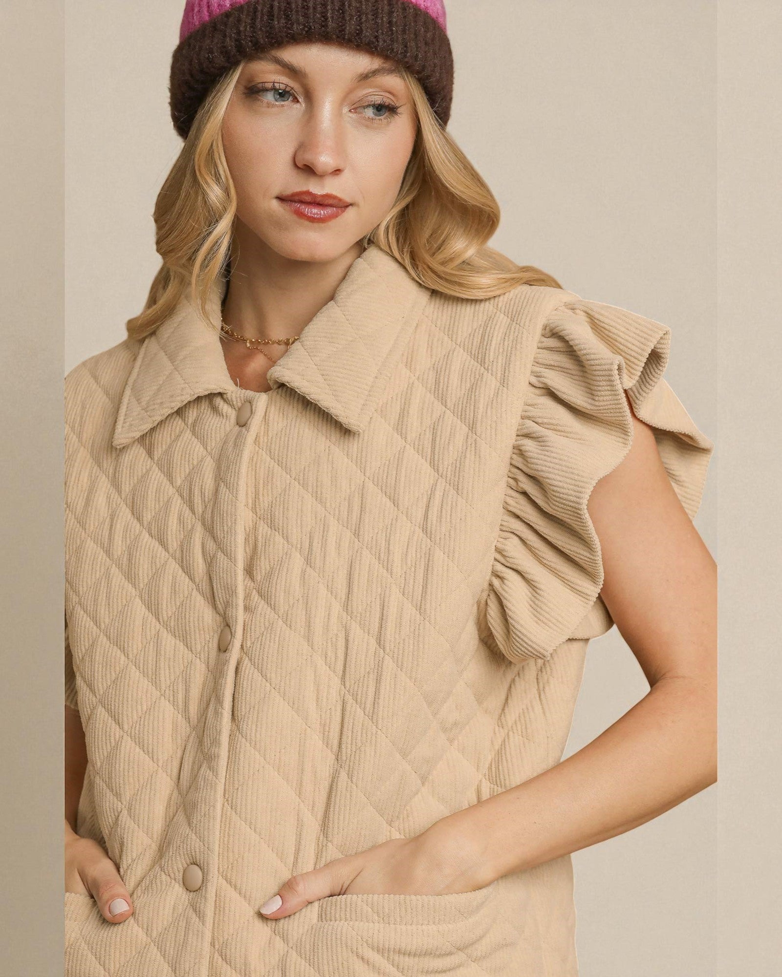 Woman wearing a beige quilted vest and pink knit hat against a neutral background
