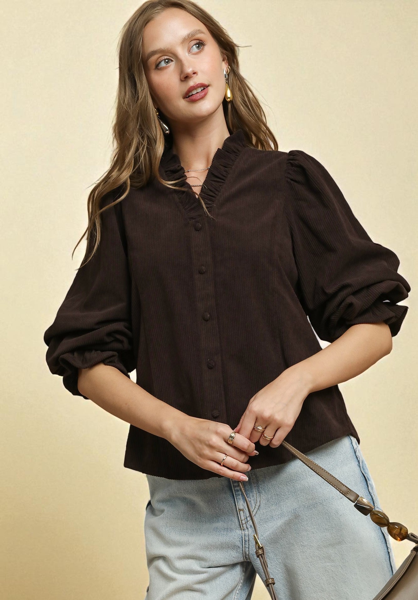 Woman wearing a dark brown blouse with puffed sleeves against a beige background