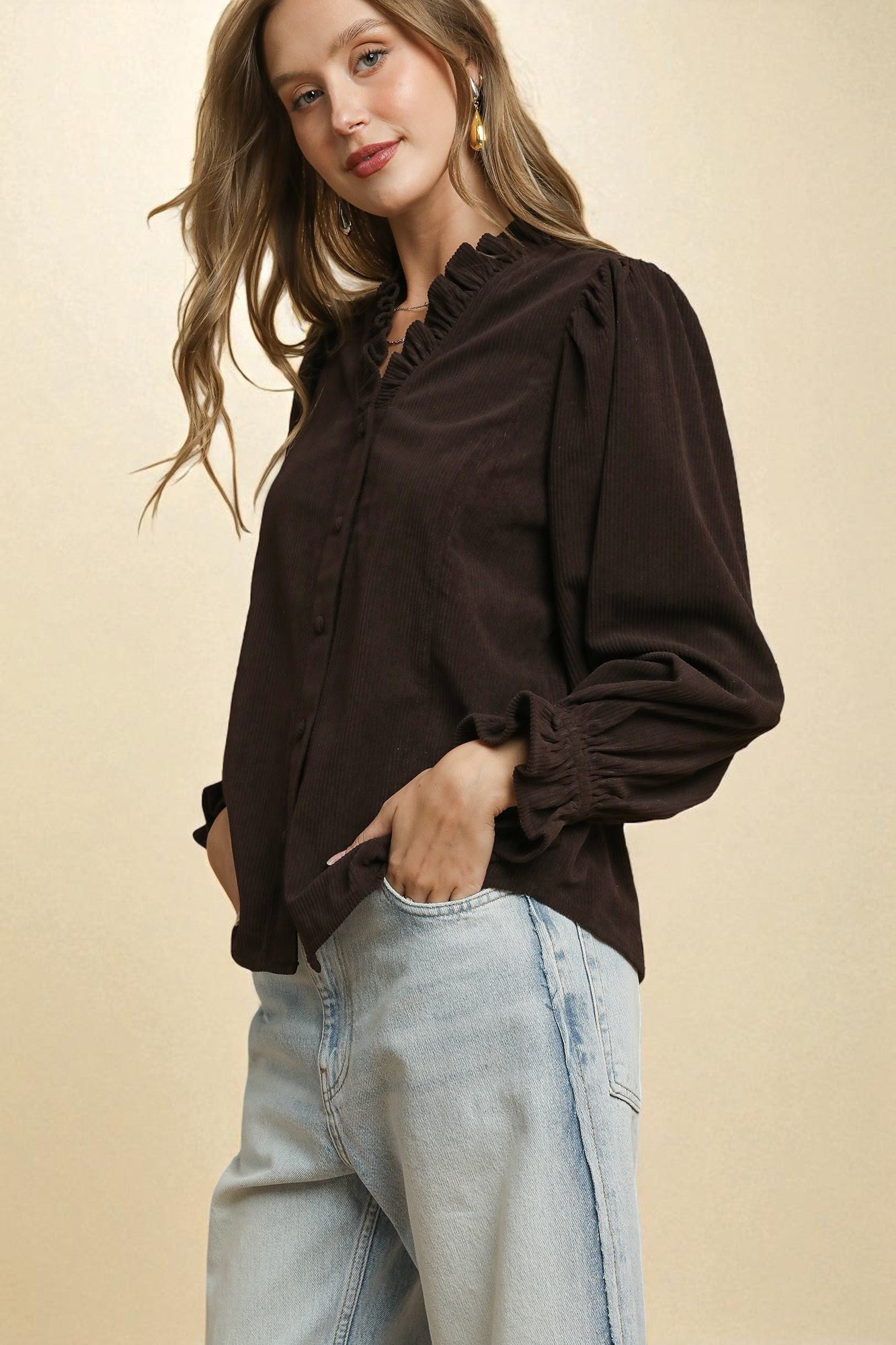 Woman wearing a brown blouse and light blue jeans against a beige background