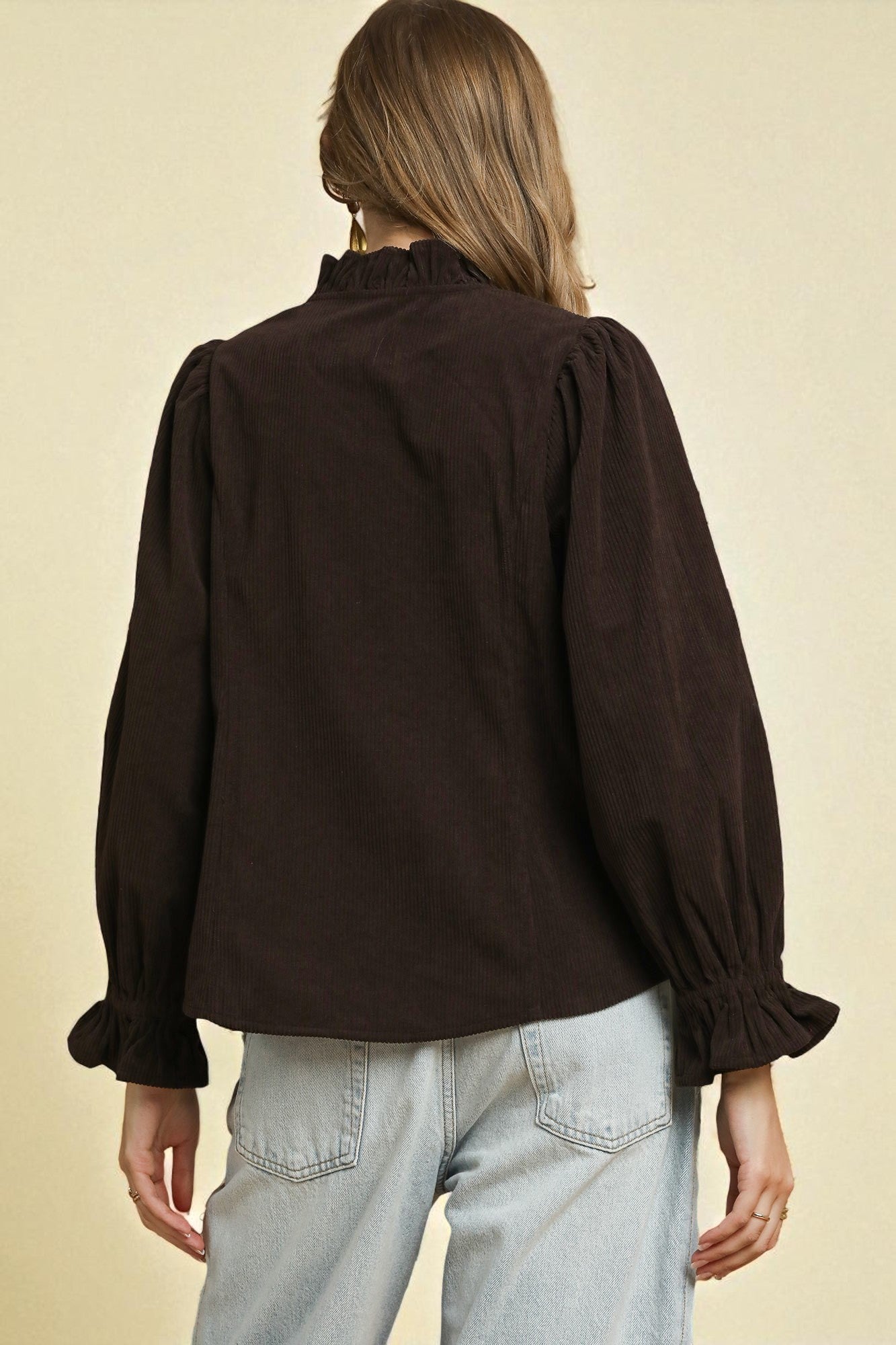 Person wearing a dark brown blouse with puffed sleeves on a beige background