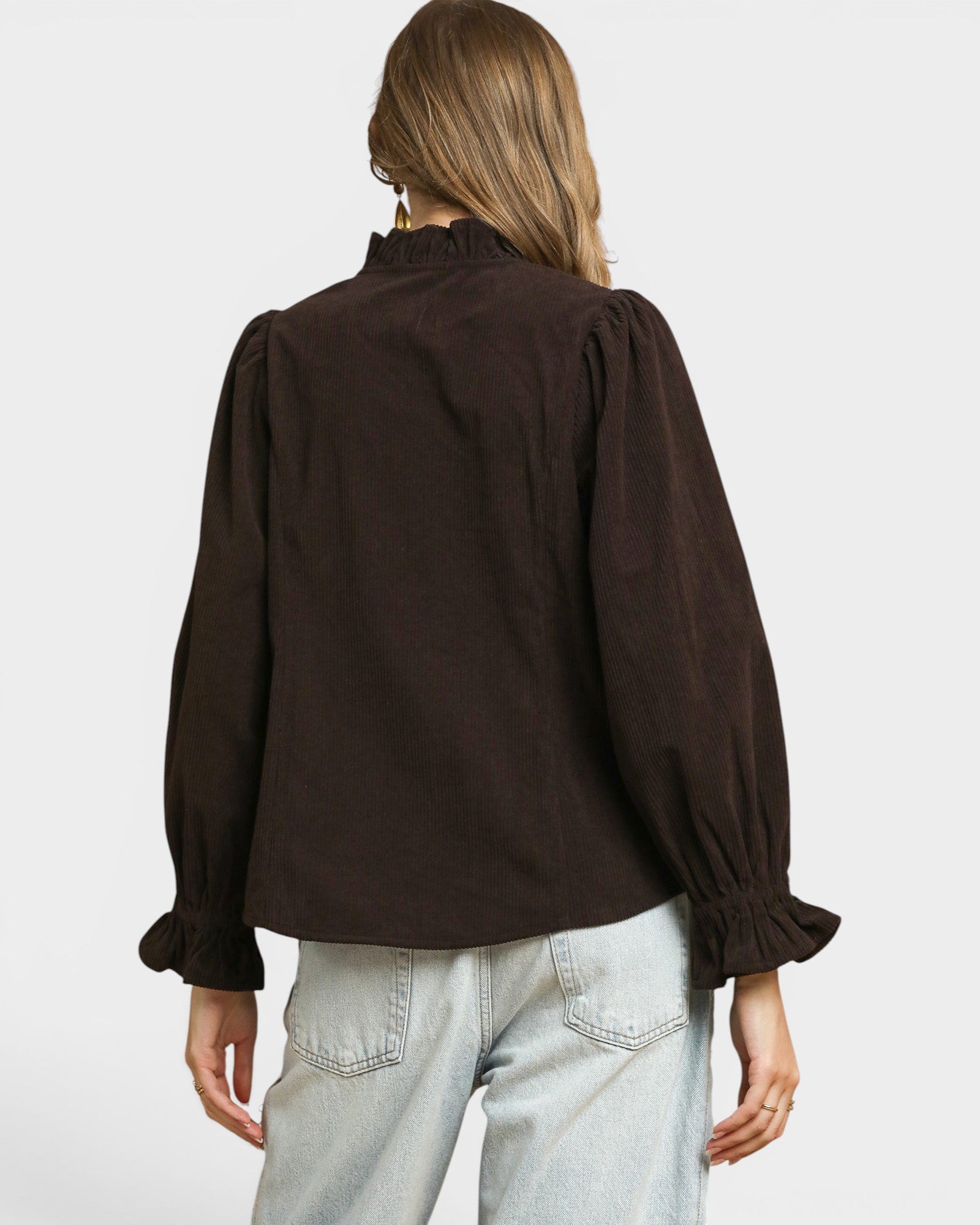 Person wearing a brown blouse with puffed sleeves on a plain background