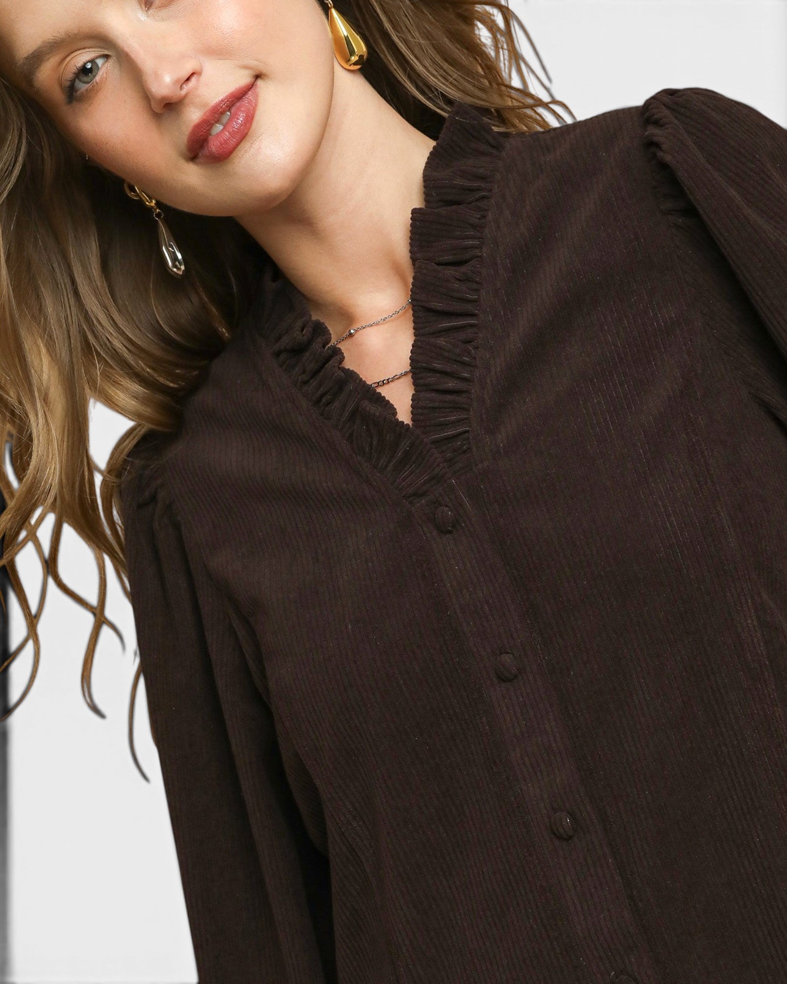 Close-up of a woman wearing a dark brown blouse with ruffled details.