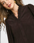 Close-up of a woman wearing a dark brown blouse with ruffled details.