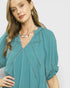 Woman wearing a teal blouse with a plain background
