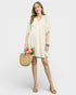 Woman in a light-colored dress holding a straw bag with flowers on a white background