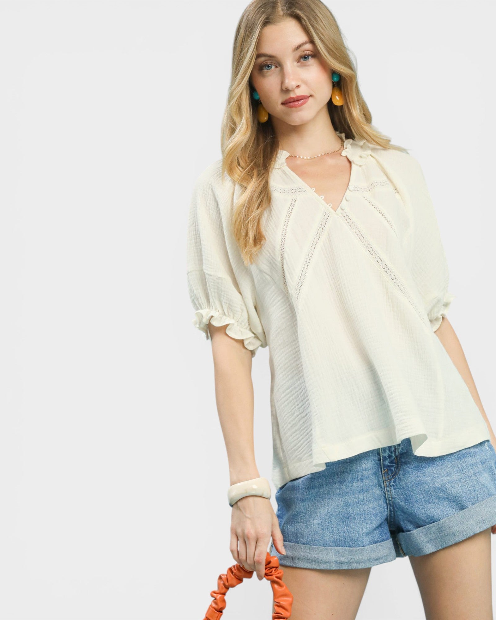 Woman wearing a light-colored blouse and denim shorts on a plain background