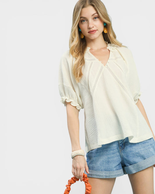 Woman wearing a light-colored blouse and denim shorts on a plain background