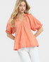 Woman wearing a coral blouse with white pants on a light background