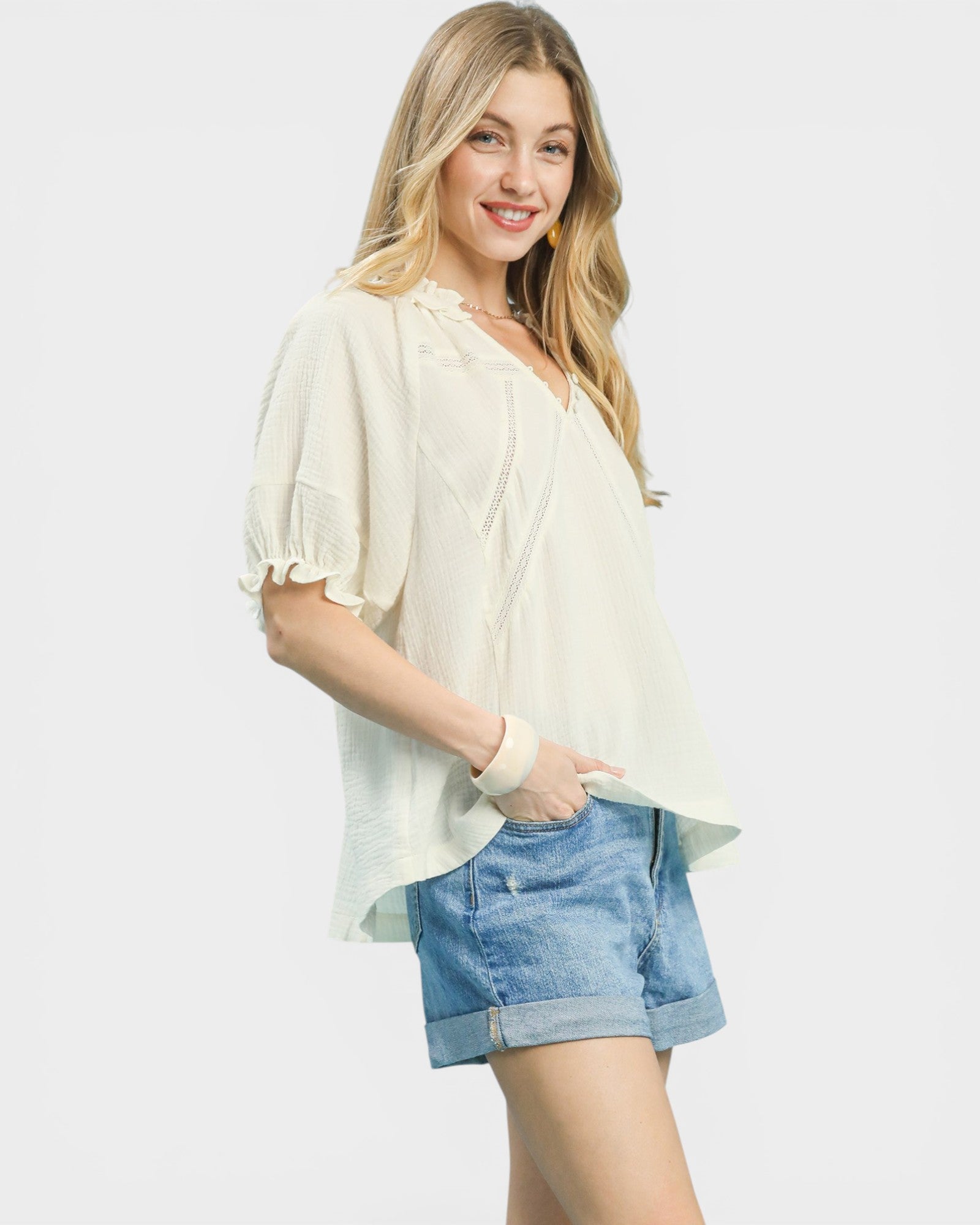 Woman wearing a light-colored blouse and denim shorts on a plain background