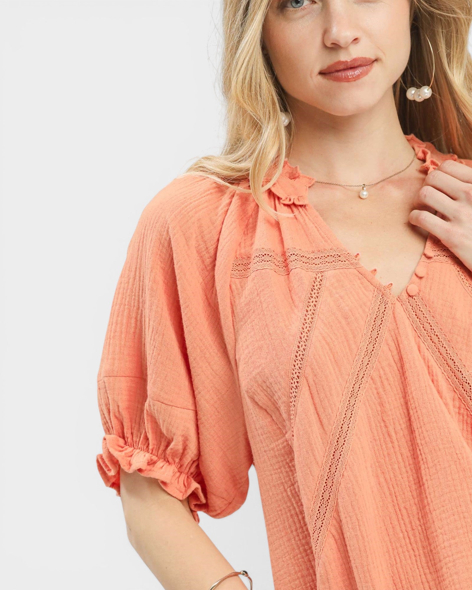 Woman wearing a peach-colored blouse with lace details on a white background
