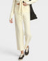 A model wearing cream wide-leg cropped pants with a matching tie-front waistband, paired with black sneakers and a black shoulder bag, against a light gray studio background.