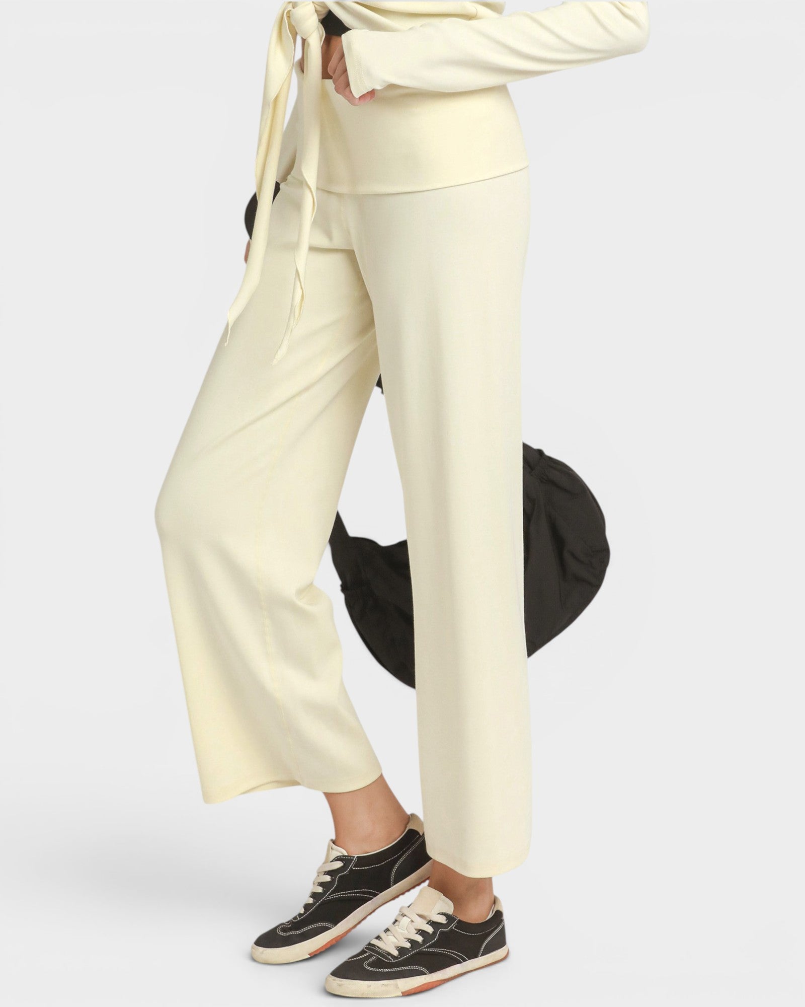 A person wearing cream-colored wide-leg cropped pants with a matching tie-front top and black low-top sneakers, photographed against a light gray studio background.