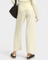 A person shown from the back wearing cream wide-leg cropped pants, a matching cream long-sleeve top, black loafers, and carrying a black shoulder bag against a light gray studio background.