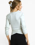 A woman shown from the back wearing a light heather gray long-sleeve top and black leggings against a plain light gray studio background.