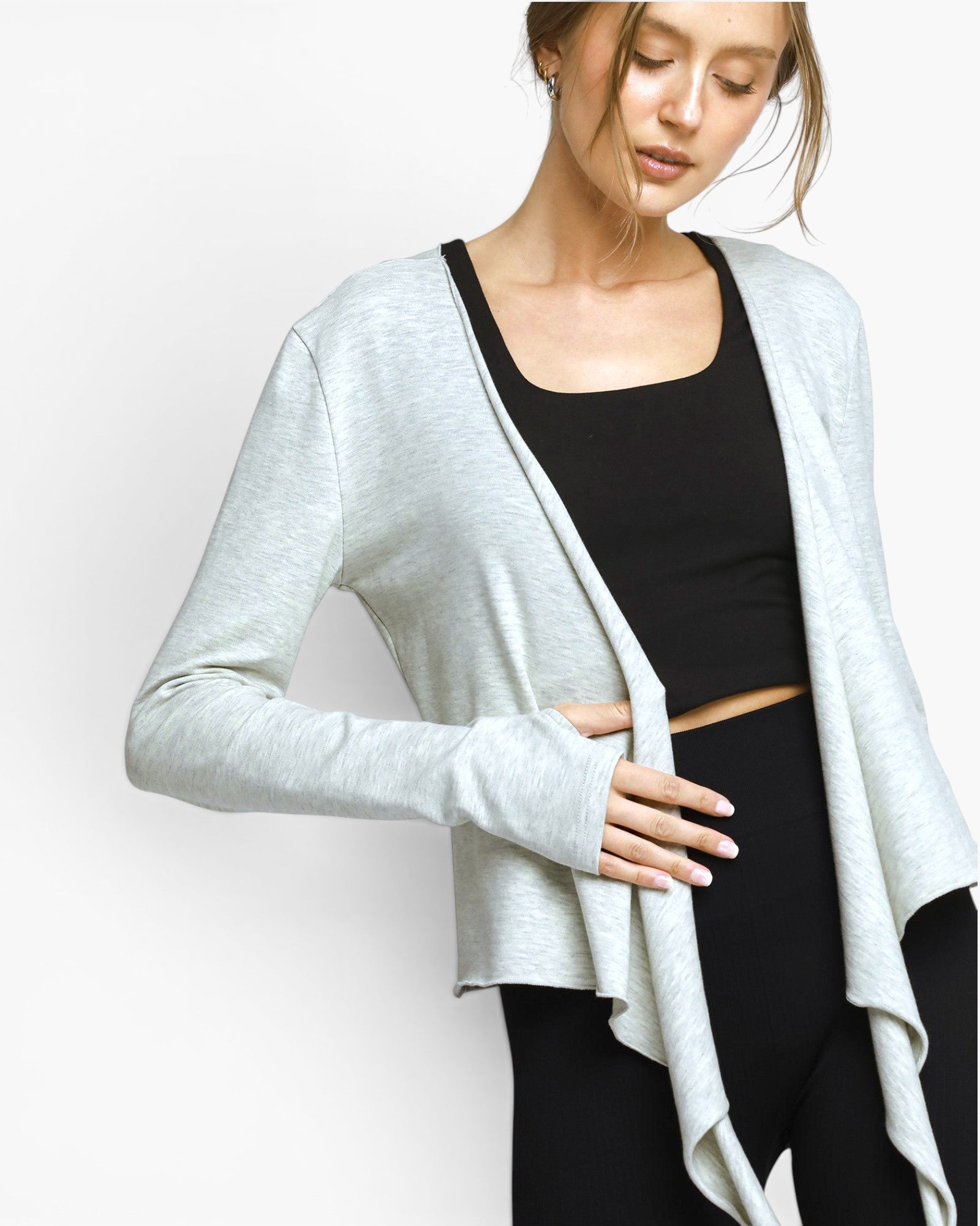 A woman wearing a light gray open-front long-sleeve cardigan over a black crop top and black leggings, photographed against a plain light gray studio background.