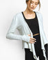 A woman wearing a light gray open-front long-sleeve cardigan over a black crop top and black leggings, photographed against a plain light gray studio background.