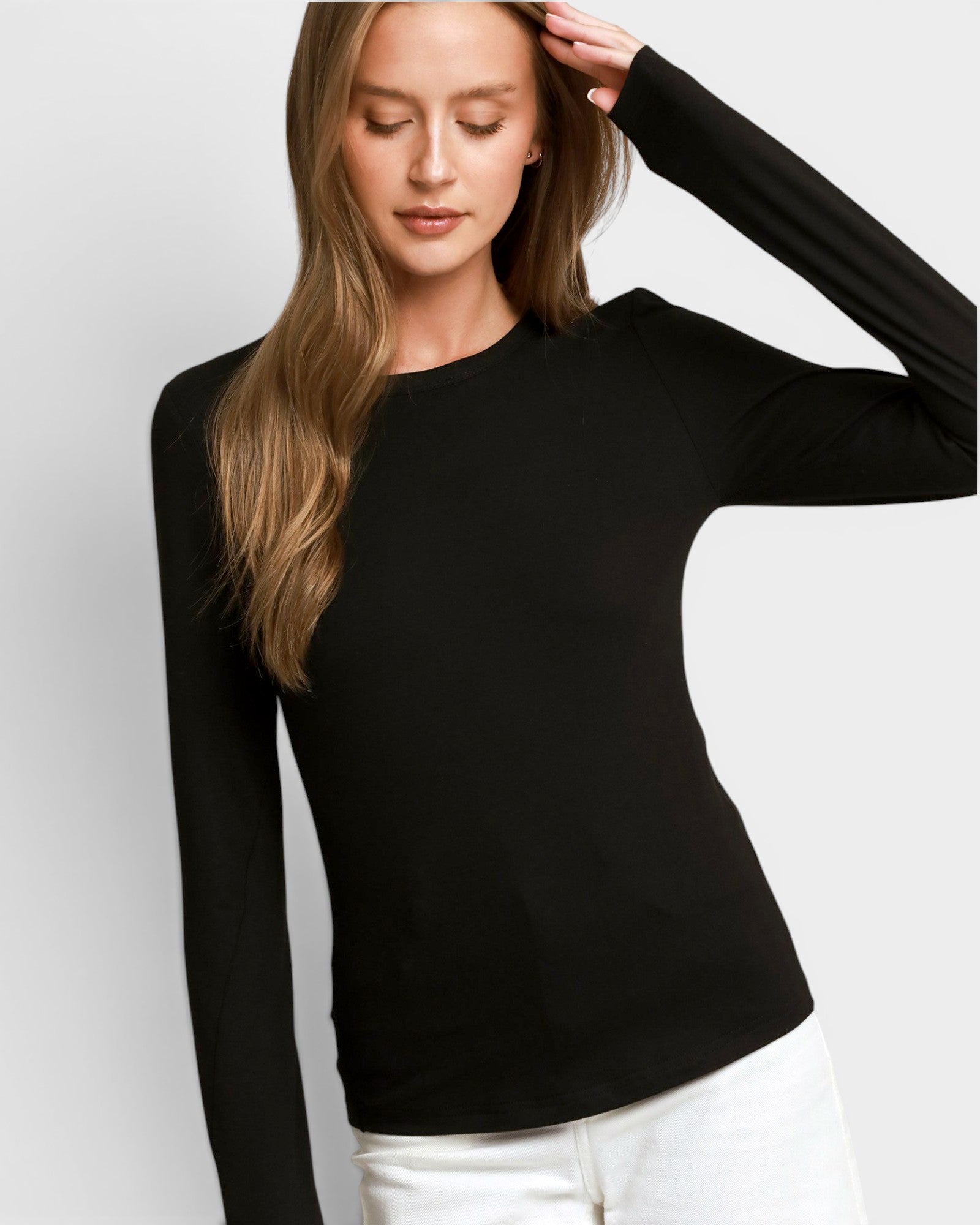 A woman wearing a black long-sleeve crewneck top and white pants, posing against a light gray studio background.