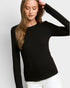 A woman wearing a black long-sleeve crewneck top and white pants, posing against a light gray studio background.