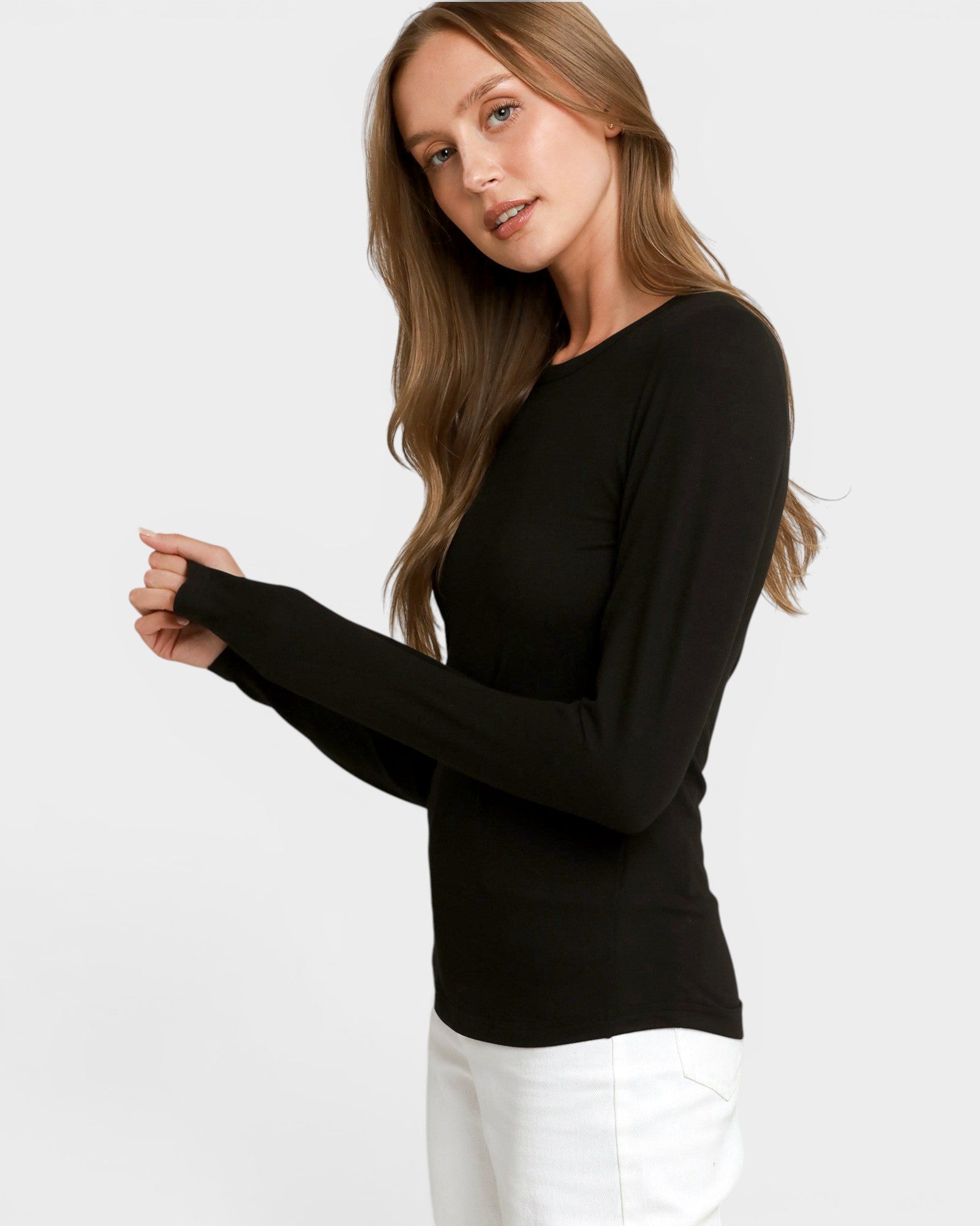 A woman modeling a black long-sleeve crewneck top with white pants against a light gray studio background.