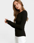 A woman modeling a black long-sleeve crewneck top with white pants against a light gray studio background.