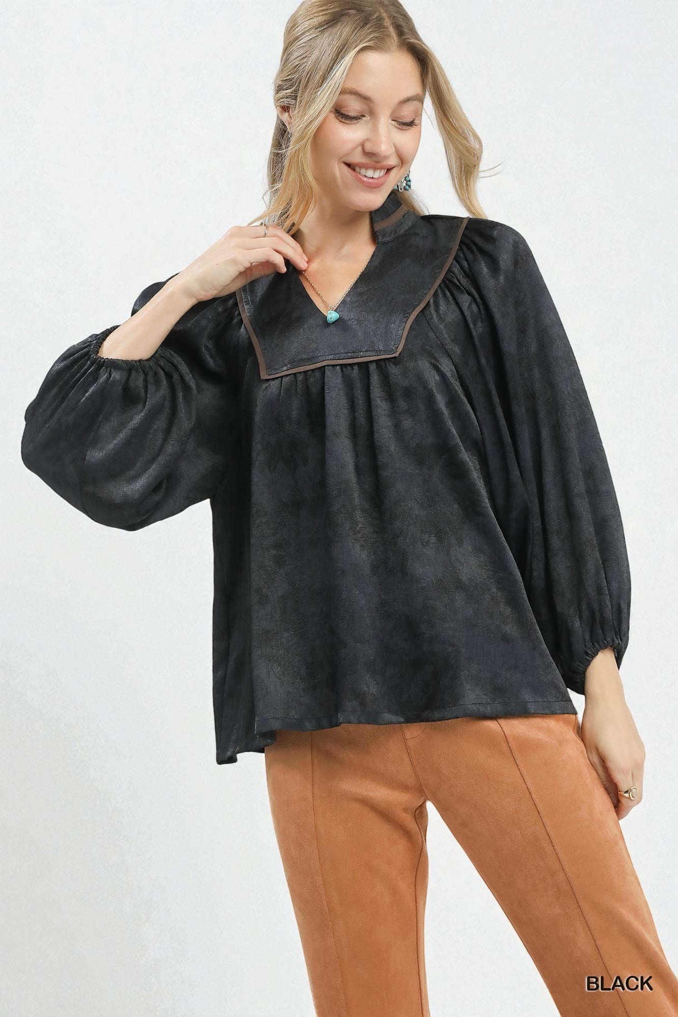 Woman wearing a black blouse with a collar and brown pants on a white background