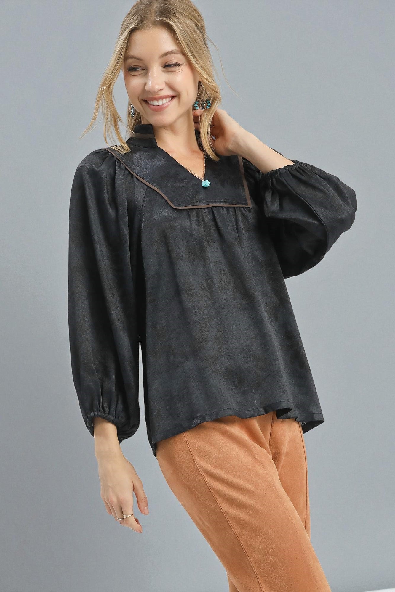 Woman wearing a black blouse with a collar and brown pants on a gray background