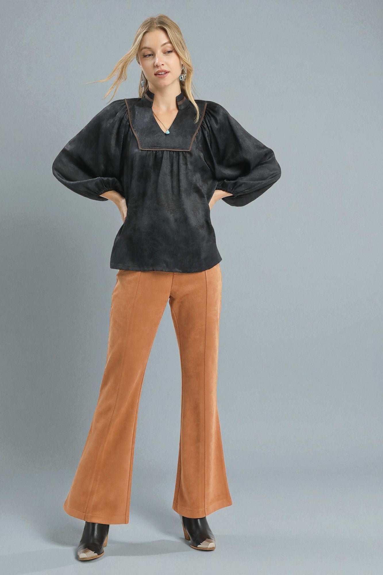 Woman wearing a black blouse and brown pants against a gray background