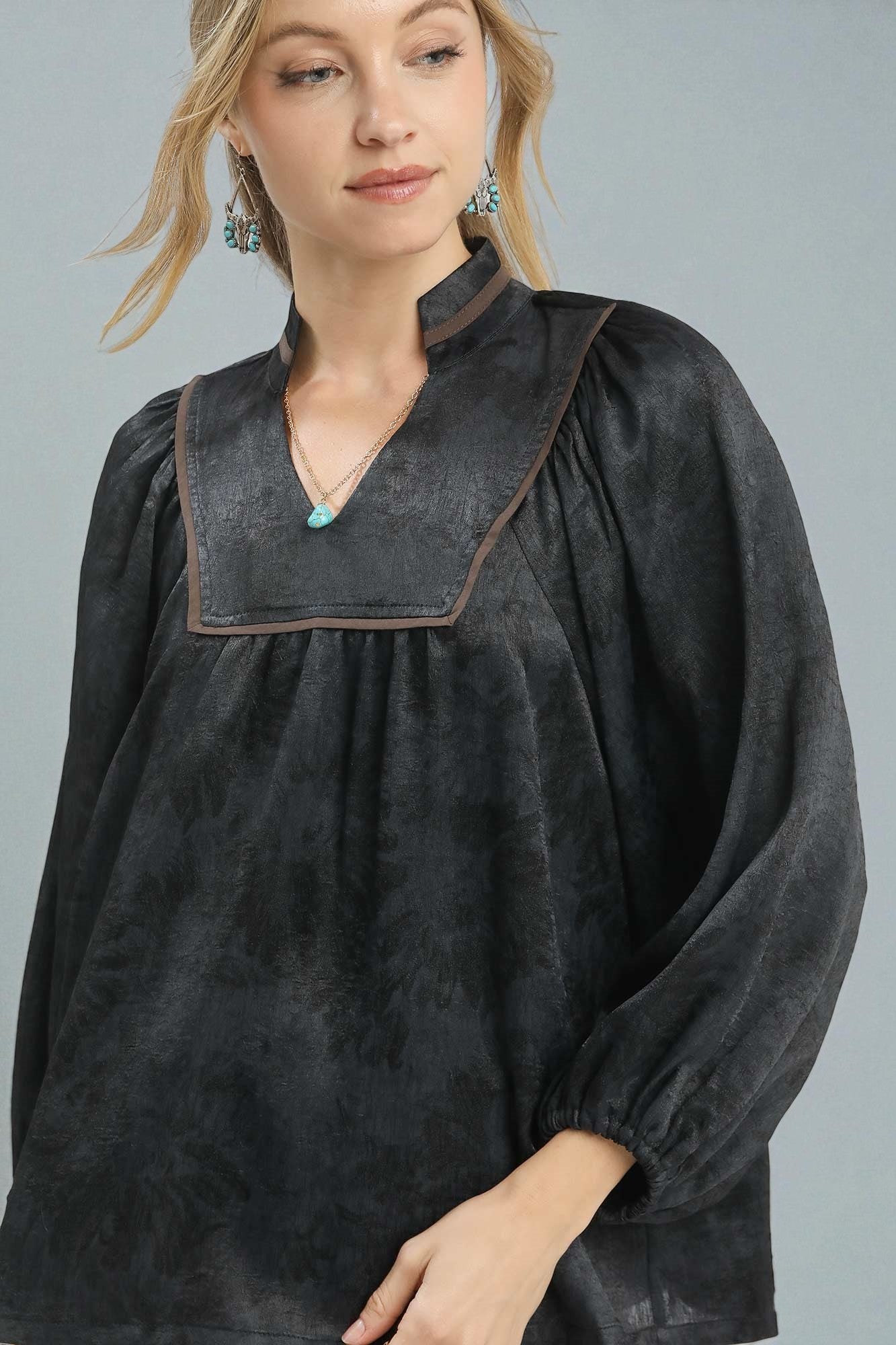 Woman wearing a black textured blouse with brown trim on a gray background