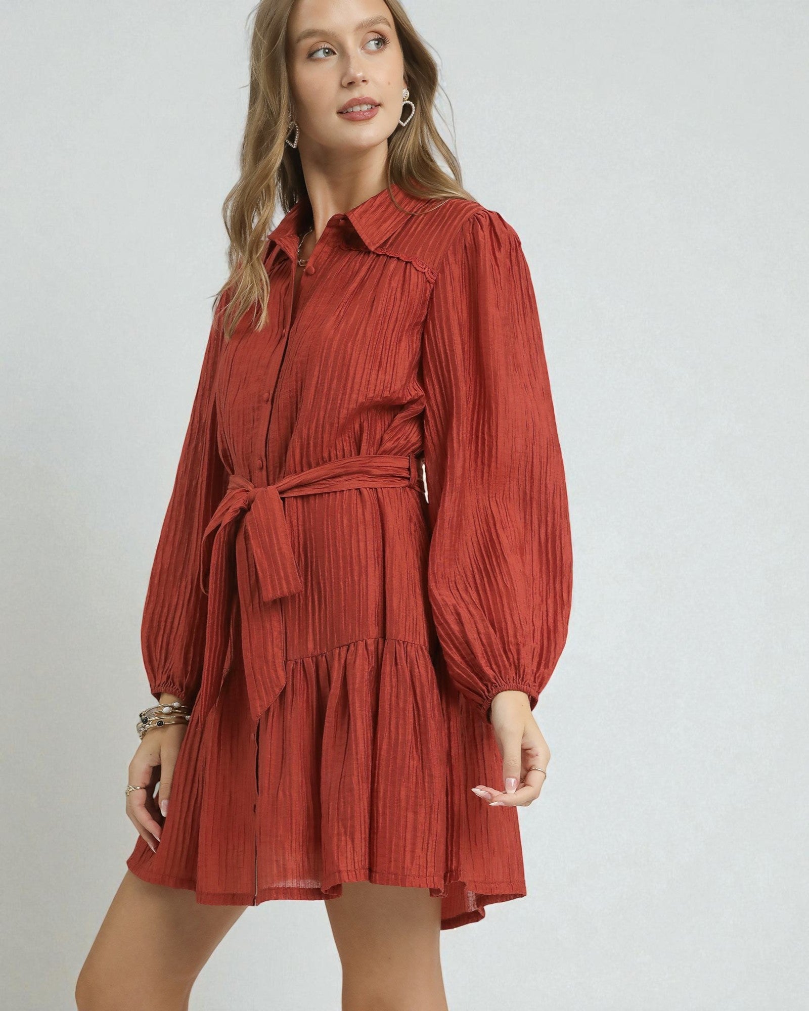 Woman wearing a rust-colored dress with a belt on a plain background