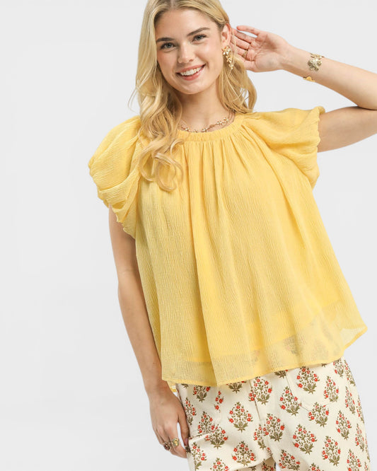 Woman wearing a yellow blouse with ruffled sleeves on a white background