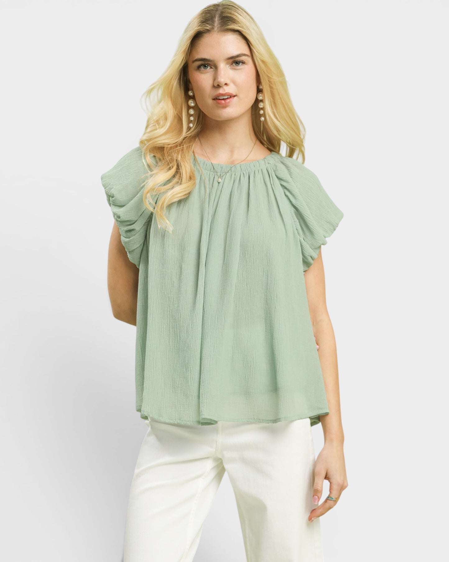 Woman wearing a light green blouse with ruffled sleeves on a white background