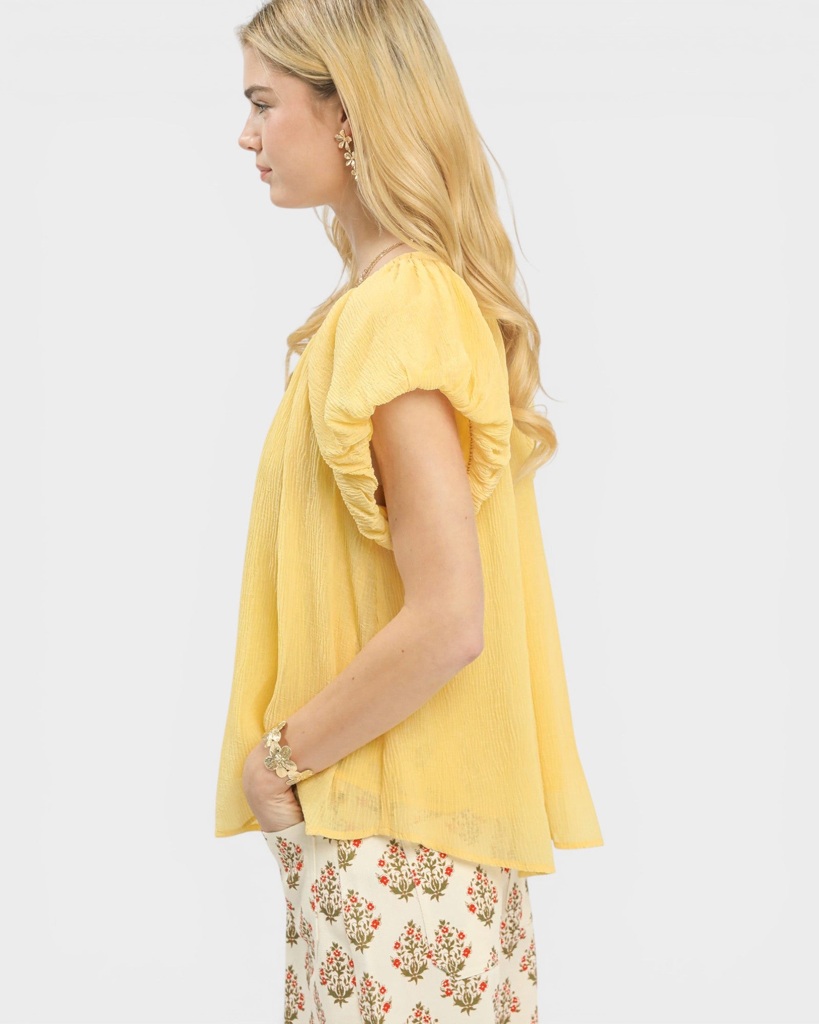 Woman wearing a yellow top with floral pants on a white background