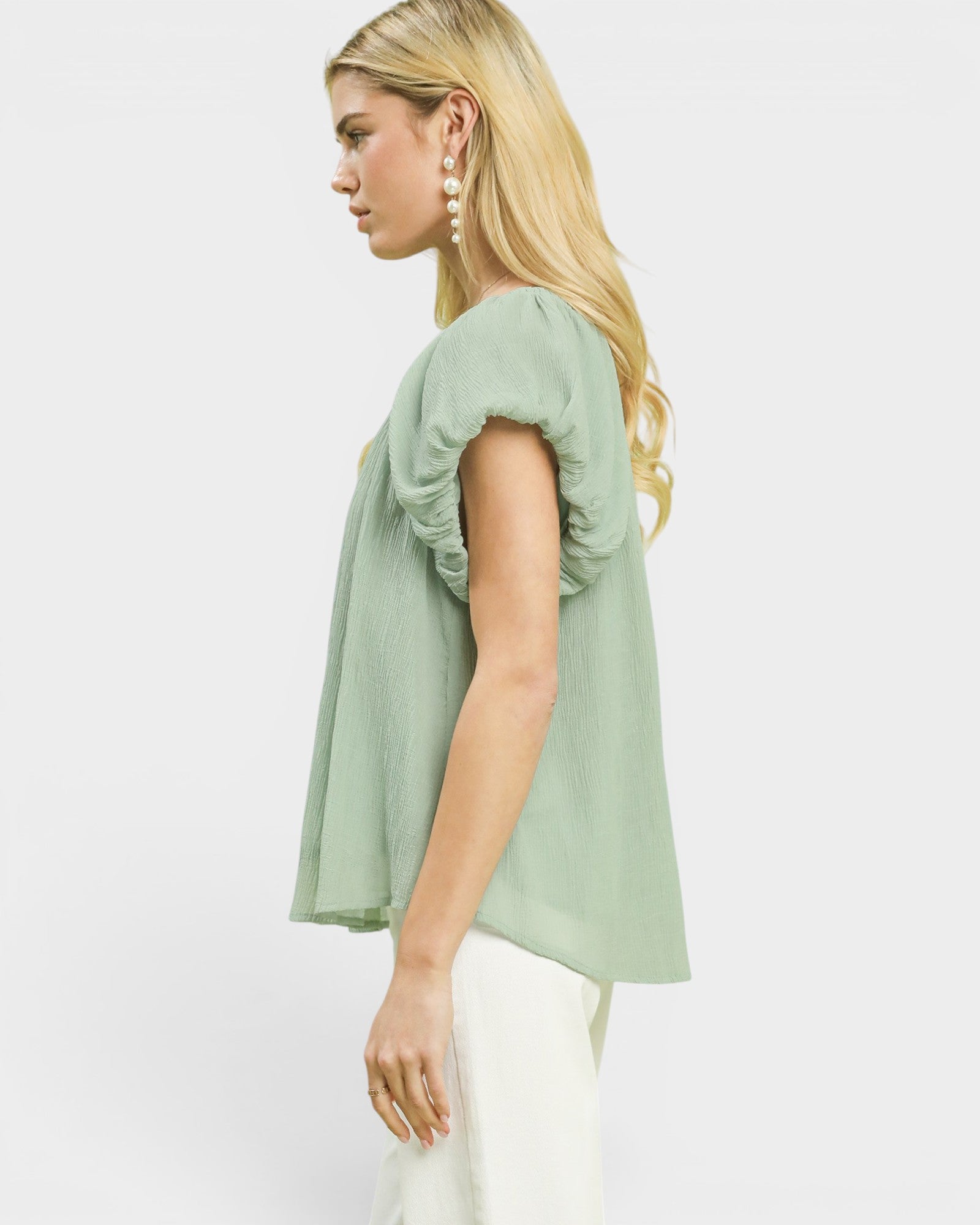 Woman wearing a light green blouse with ruched sleeves on a white background