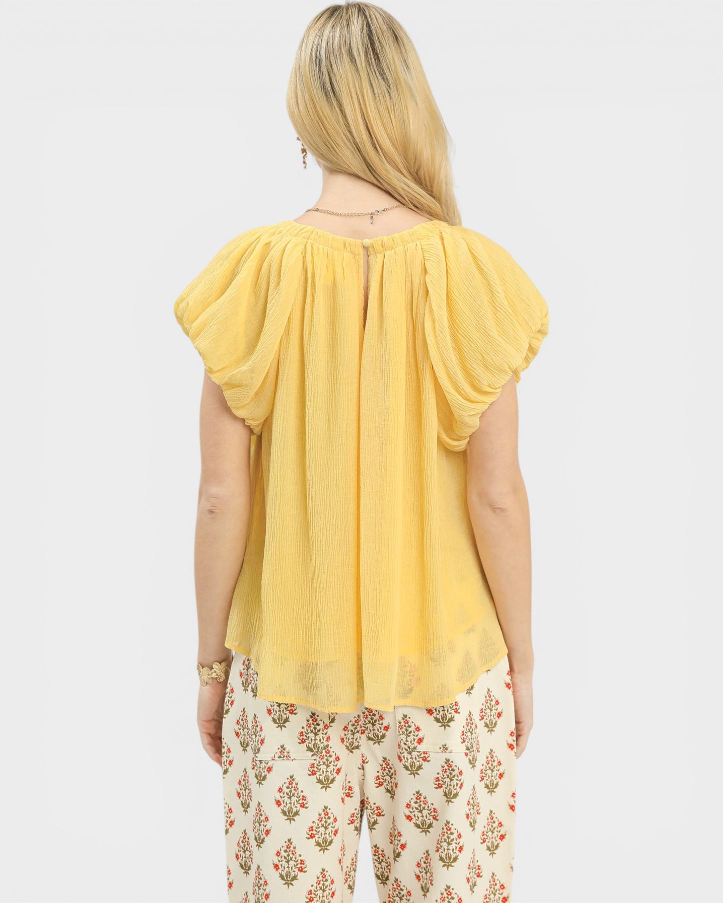 Woman wearing a yellow top and floral pants on a white background