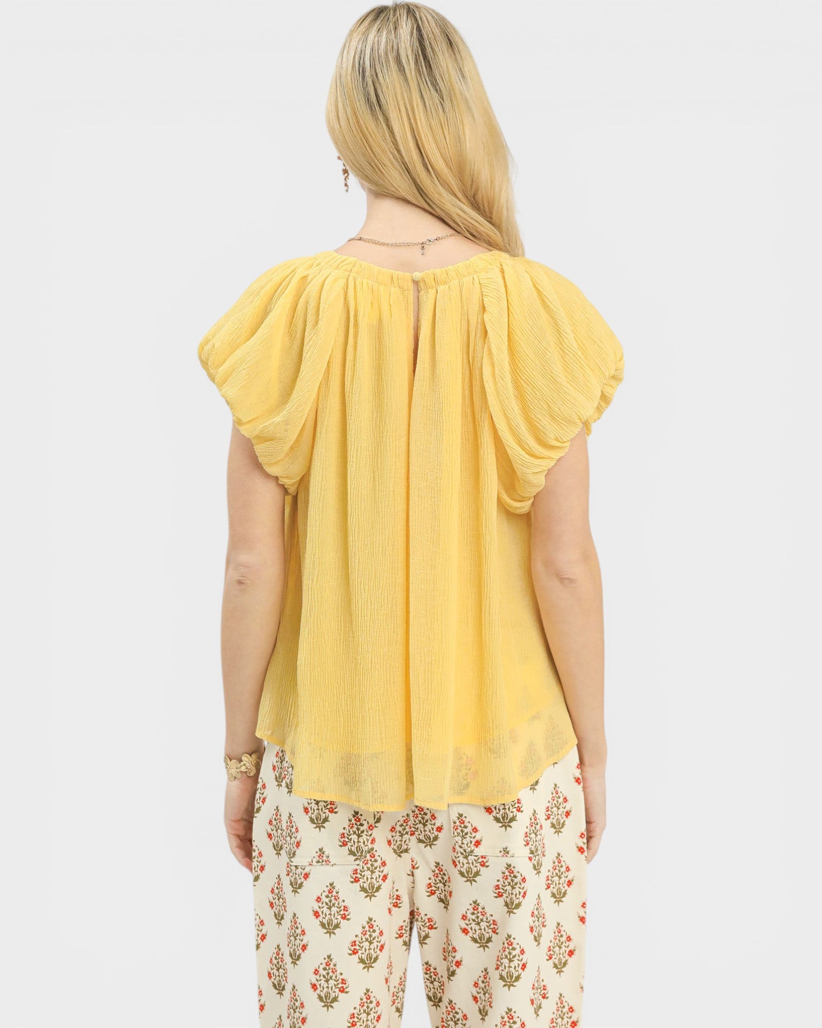 Woman wearing a yellow top and floral pants on a white background