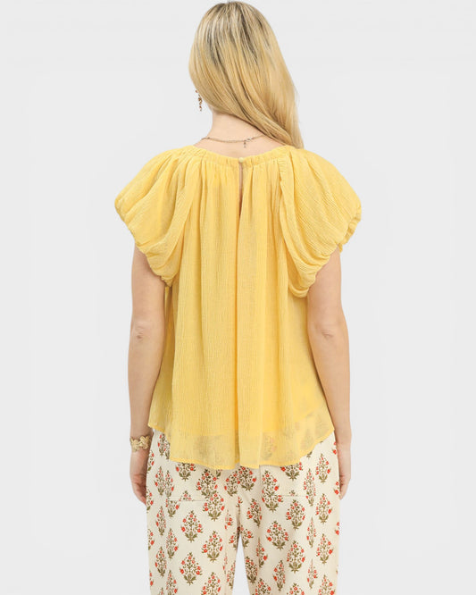 Woman wearing a yellow top and floral pants on a white background