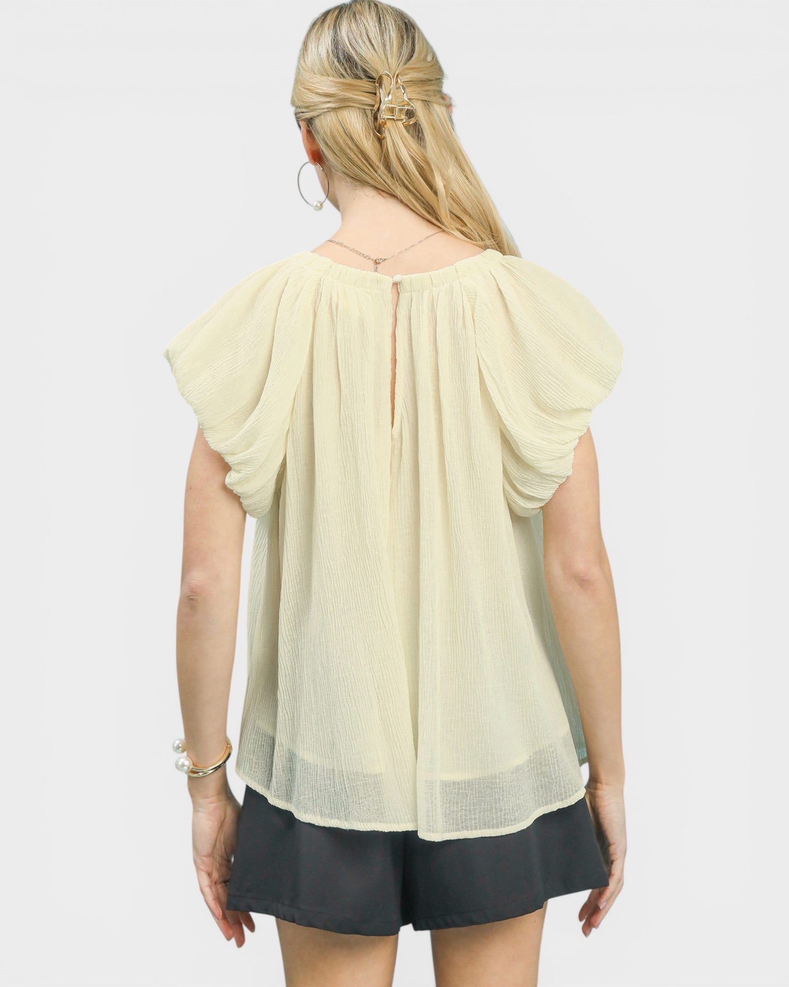 Woman wearing a light-colored blouse with ruffled sleeves on a white background