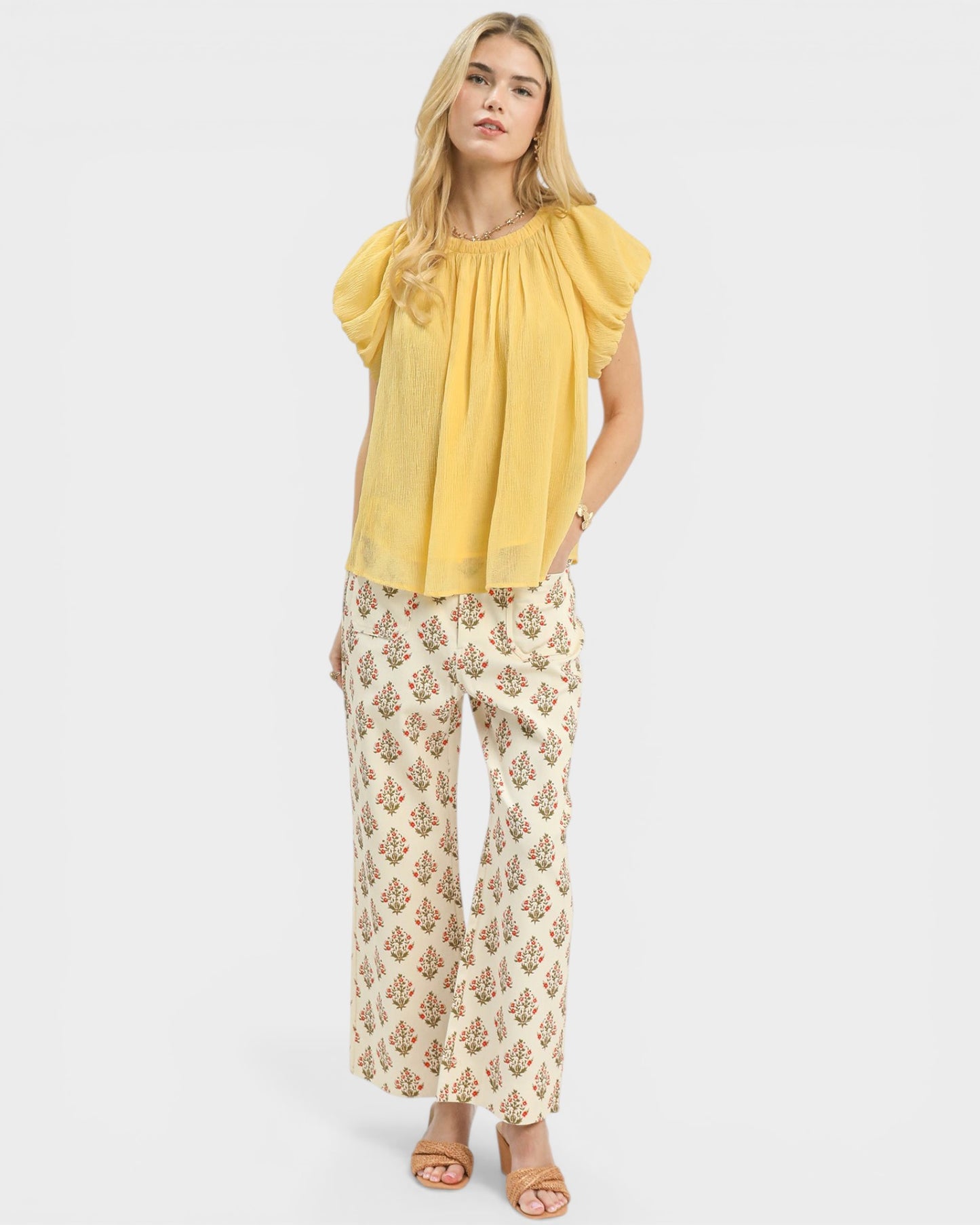 Woman wearing a yellow blouse and floral pants on a white background