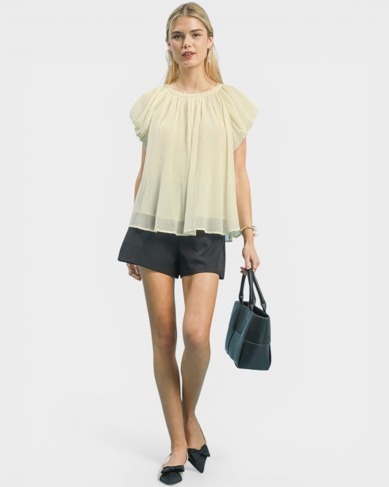 Woman wearing a light-colored blouse and black shorts, holding a handbag on a white background