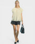 Woman wearing a light-colored blouse and black shorts, holding a handbag on a white background