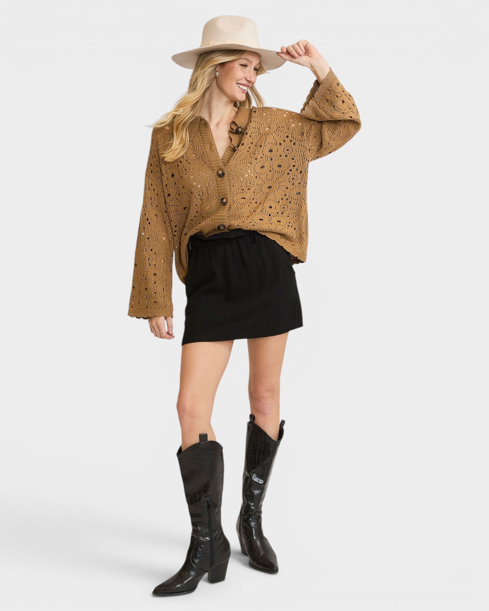 Woman wearing a brown cardigan, black skirt, and black boots on a white background