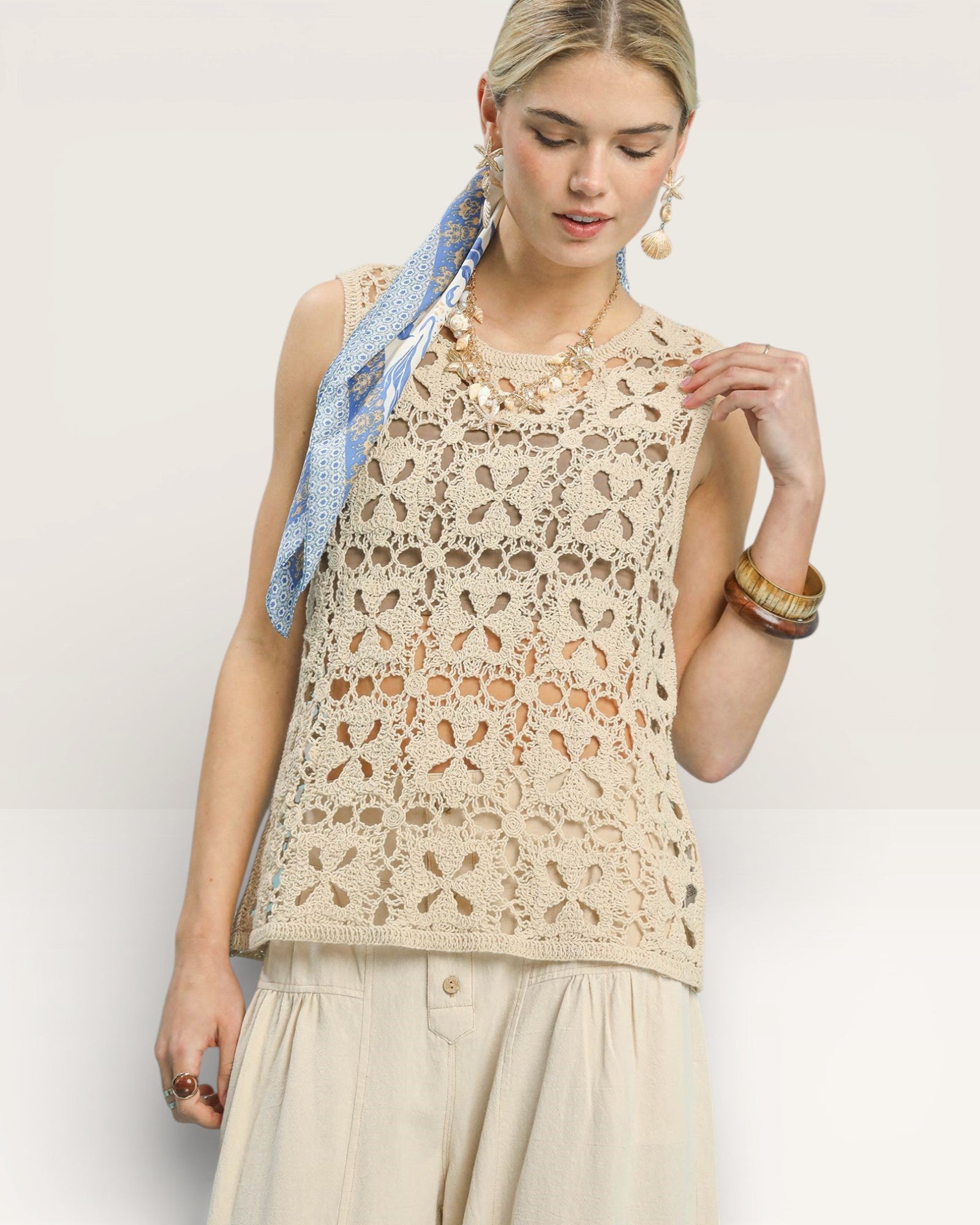 Woman wearing a beige lace top with a blue scarf on a white background