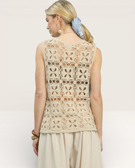 Woman wearing a beige sleeveless crochet top with a plain background