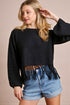 Woman wearing a black fringed sweater and denim shorts on a beige background