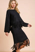 Woman wearing a black fringe sweater and skirt set on a beige background