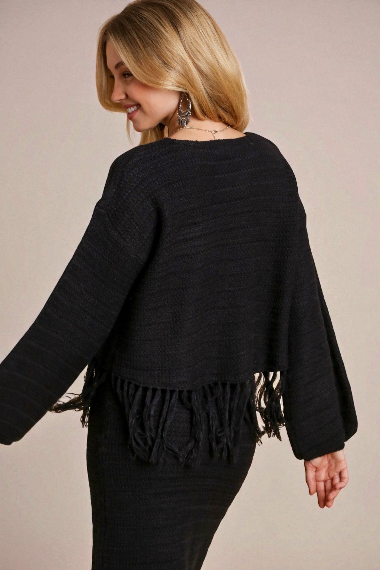Woman wearing a black fringed sweater against a beige background